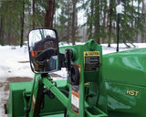 A green tractor with a rear view mirror, positioned in a rural setting, showcasing its sturdy design and vibrant color.